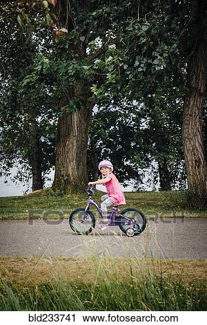 Stock Image - Mixed Race girl riding bicycle with training wheels. Fotosearch