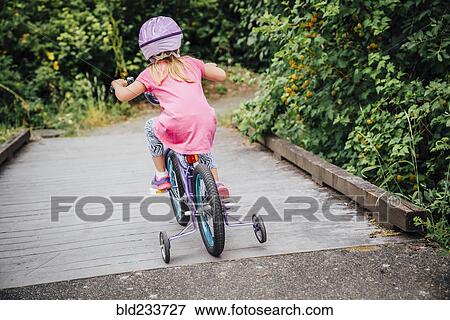 Stock Photo - Mixed Race girl riding bicycle with training wheels. Fotosearch