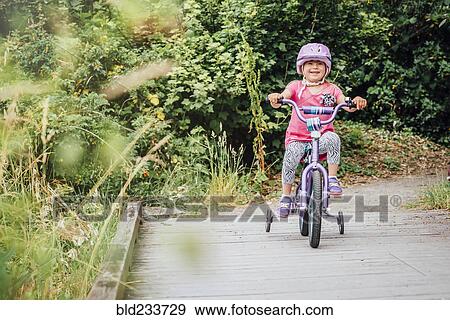 Stock Photo - Mixed Race girl riding bicycle with training wheels. Fotosearch