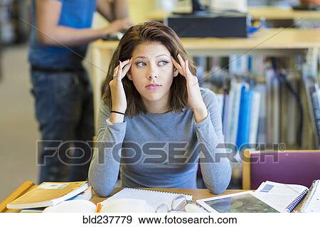 Mixed Race girl rubbing temples in library View Large Photo Image Stock Photo - Mixed Race girl rubbing temples in library. Fotosearch