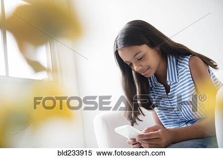 Mixed Race girl sitting in armchair texting on cell phone View Large Photo Image Stock Photography - Mixed Race girl sitting in armchair texting on cell phone. Fotosearch