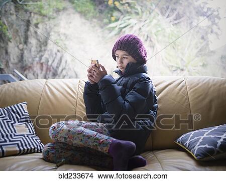 Picture - Mixed Race girl sitting on sofa texting on cell phone. Fotosearch