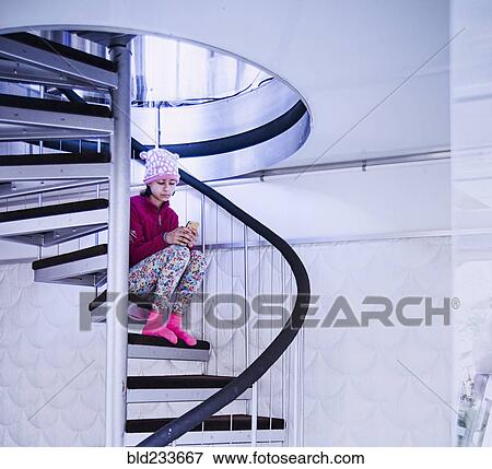 Stock Photo - Mixed Race girl sitting on spiral staircase texting on cell phone. Fotosearch