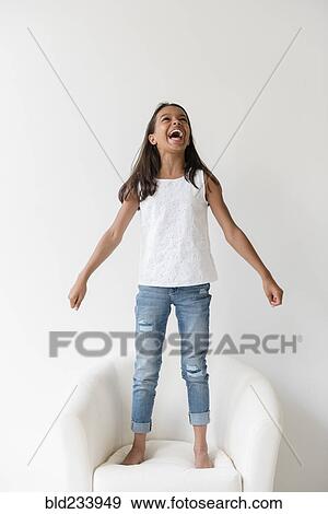 Mixed Race girl standing barefoot on armchair and shouting View Large Photo Image Stock Photo - Mixed Race girl standing barefoot on armchair and shouting. Fotosearch
