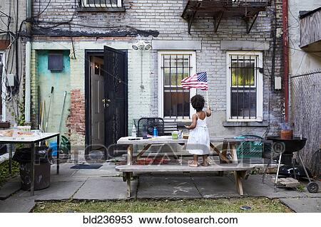 Stock Image - Mixed Race girl standing on backyard bench waving American flag. Fotosearch
