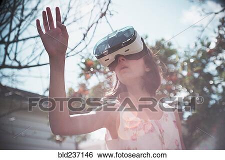Stock Photograph - Mixed Race girl using virtual reality goggles outdoors. Fotosearch
