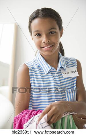 Stock Image - Mixed Race girl volunteering and carrying clothing. Fotosearch