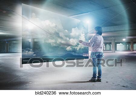 Stock Photograph - Mixed Race girl watching clouds on virtual screen in parking garage. Fotosearch