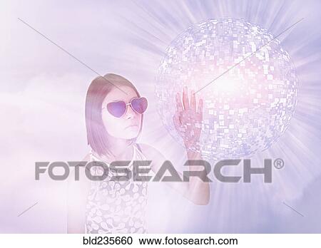 Stock Image - Mixed Race girl wearing sunglasses touching hovering pixel sphere. Fotosearch