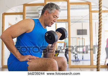 Mixed Race man curling dumbbell in gymnasium View Large Photo Image Picture - Mixed Race man curling dumbbell in gymnasium. Fotosearch