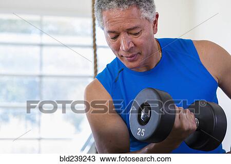 Stock Image - Mixed Race man curling dumbbell. Fotosearch