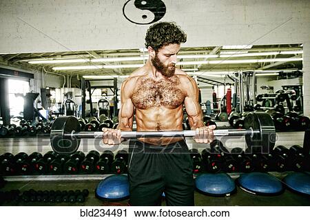 Stock Image - Mixed Race man lifting barbell in gymnasium. Fotosearch