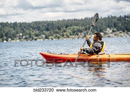 Stock Image - Mixed Race man paddling kayak. Fotosearch