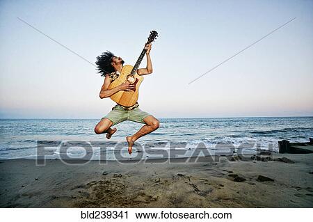Mixed Race man playing guitar and jumping at beach View Large Photo Image Stock Image - Mixed Race man playing guitar and jumping at beach. Fotosearch