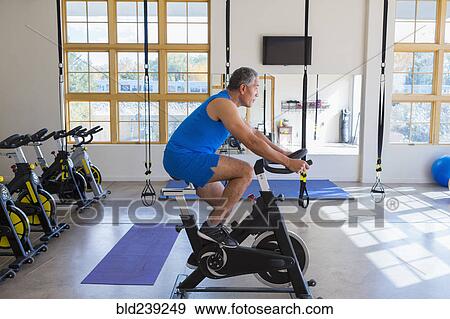 Stock Photo - Mixed Race man riding stationary bicycle in gymnasium. Fotosearch