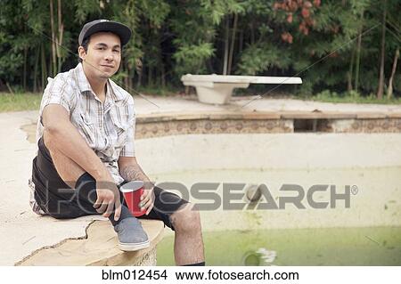 Mixed race man sitting on edge of disused swimming pool View Large Photo Image Picture - Mixed race man sitting on edge of disused swimming pool. Fotosearch