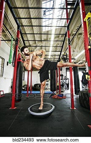 Stock Image - Mixed Race man standing on balance trainer in gymnasium. Fotosearch
