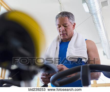 Stock Image - Mixed Race man texting on cell phone in gymnasium. Fotosearch