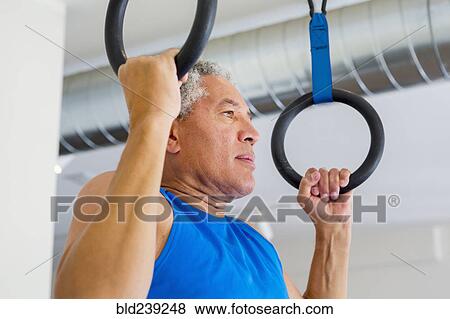Stock Photo - Mixed Race man using pull-up rings in gymnasium. Fotosearch