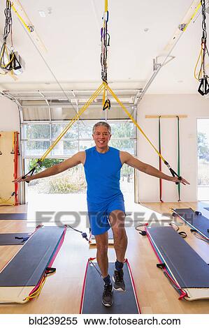 Stock Photography - Mixed Race man using resistance bands in gymnasium. Fotosearch