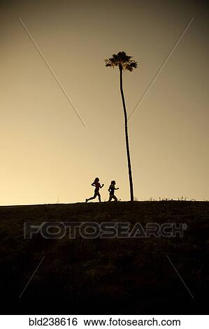 Stock Photograph - Mixed Race mother and daughter running near palm tree. Fotosearch
