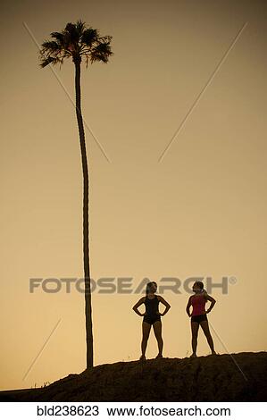 Stock Image - Mixed Race mother and daughter standing near palm tree. Fotosearch