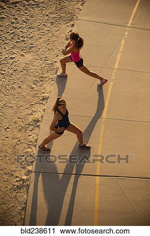 Stock Image - Mixed Race mother and daughter stretching on path at beach. Fotosearch
