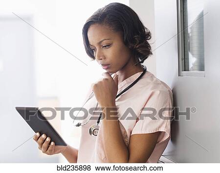 Stock Photo - Mixed Race nurse using digital tablet leaning on door. Fotosearch
