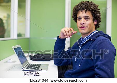 Picture - Mixed Race student using laptop in library. Fotosearch
