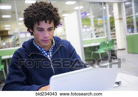 Stock Image - Mixed Race student using laptop in library. Fotosearch