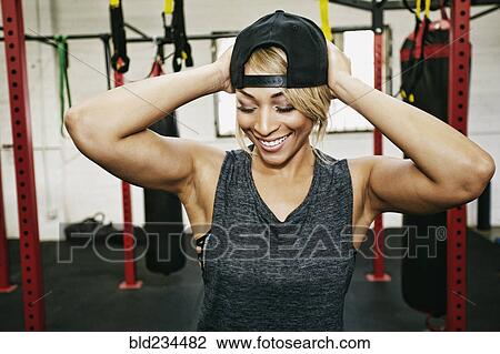 Stock Image - Mixed Race woman adjusting hat in gymnasium. Fotosearch
