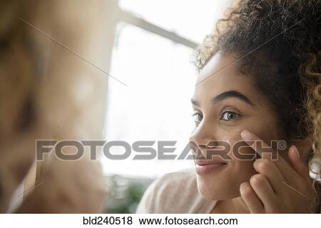 Stock Photo - Mixed Race woman applying lotion to cheek. Fotosearch