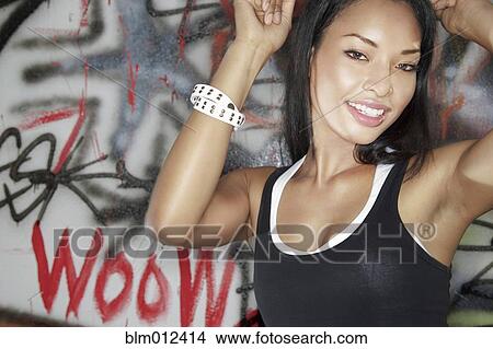 Picture - Mixed race woman dancing near graffitied wall. Fotosearch