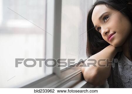 Stock Image - Mixed Race woman daydreaming at window. Fotosearch
