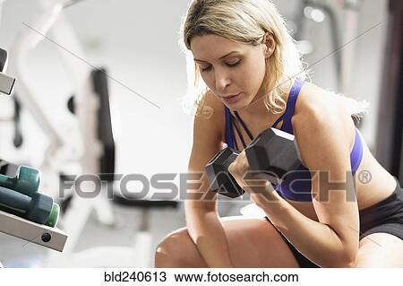 Stock Image - Mixed Race woman doing curls with dumbbell. Fotosearch