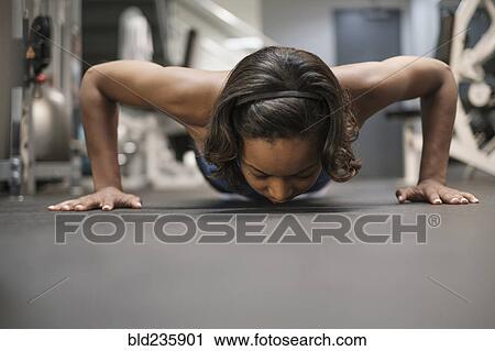 Stock Image - Mixed Race woman doing push-up on floor at gymnasium. Fotosearch