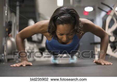 Stock Image - Mixed Race woman doing push-up on floor at gymnasium. Fotosearch