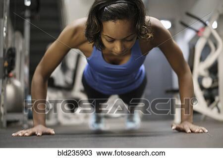 Stock Image - Mixed Race woman doing push-up on floor at gymnasium. Fotosearch