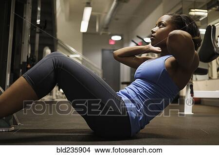 Picture - Mixed Race woman doing sit-up on floor at gymnasium. Fotosearch