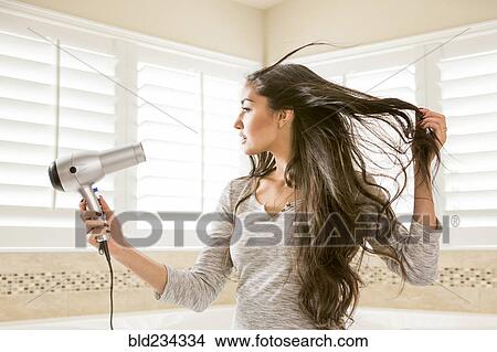 Picture - Mixed Race woman drying hair in bathroom. Fotosearch