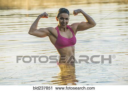 Stock Image - Mixed Race woman flexing muscles in lake. Fotosearch