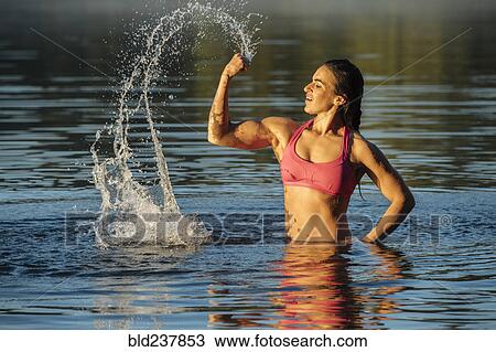 Stock Image - Mixed Race woman flexing muscles in lake. Fotosearch