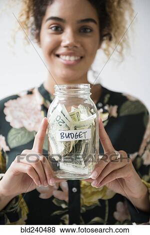 Stock Photo - Mixed Race woman holding jar of budget money. Fotosearch
