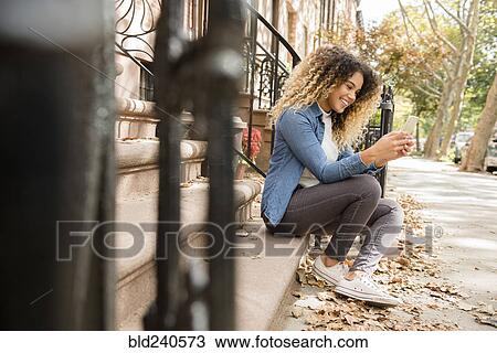 Stock Image - Mixed Race woman in city texting on cell phone. Fotosearch