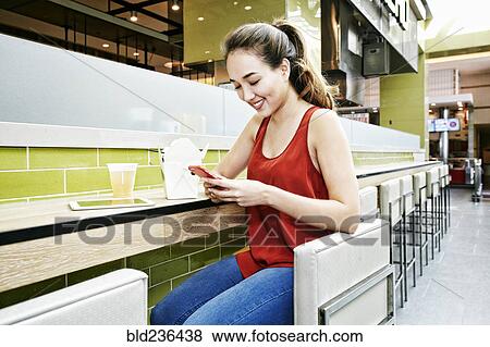 Stock Photo - Mixed Race woman in food court texting on cell phone. Fotosearch