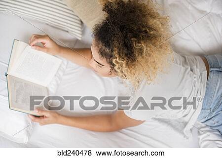 Stock Photo - Mixed Race woman laying on bed reading book. Fotosearch
