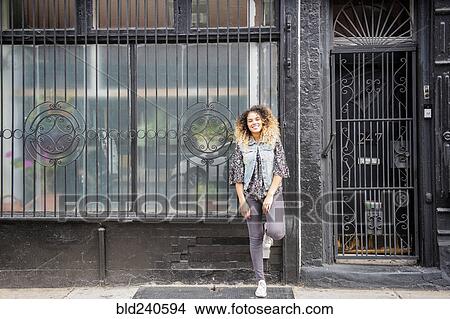 Mixed Race woman leaning on gated window in city View Large Photo Image Picture - Mixed Race woman leaning on gated window in city. Fotosearch