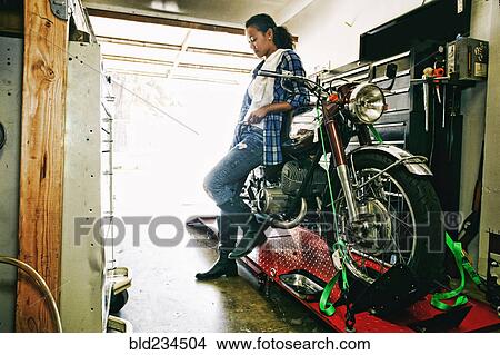 Mixed Race woman leaning on motorcycle in garage View Large Photo Image Picture - Mixed Race woman leaning on motorcycle in garage. Fotosearch