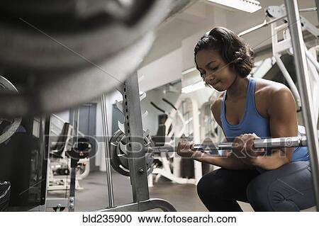 Stock Image - Mixed Race woman lifting barbell at gymnasium. Fotosearch