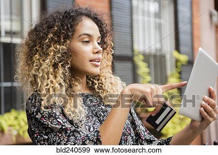 Stock Photo - Mixed Race woman online shopping with digital tablet in city. Fotosearch